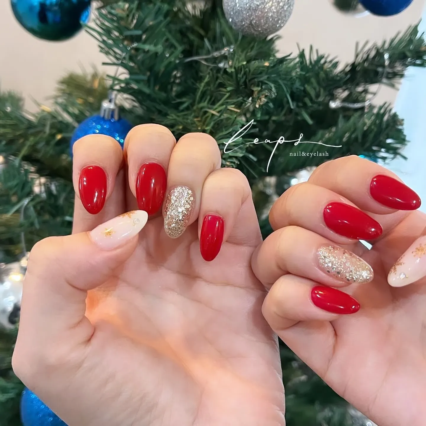 クリスマスツリーを背景にした、赤と白とラメのネイル